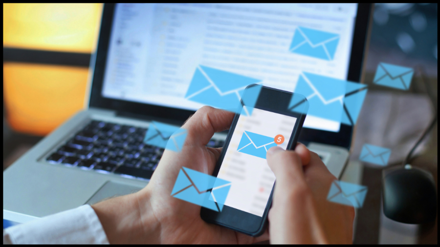 hoto of a person holding a mobile phone that has a blue envelope on the screen showing 5 unread email messages while several blue vector envelopes float around the phone screen. Image from Canva Pro.